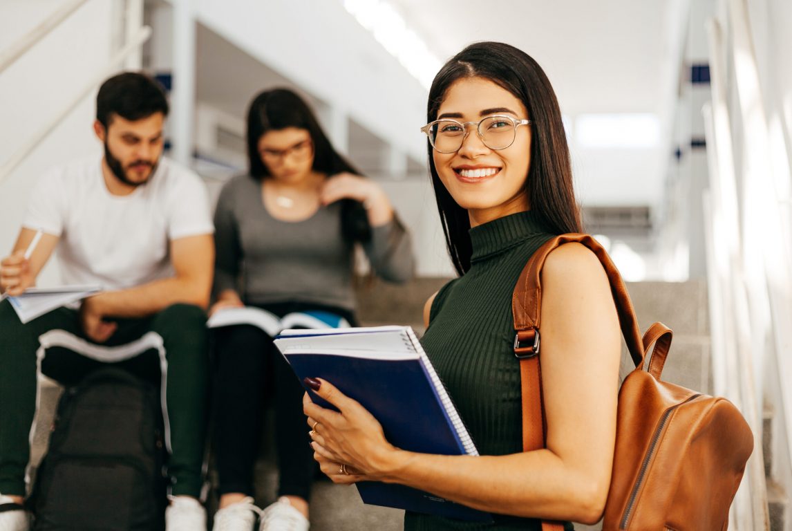 Portrait of young Brazilian student with backpack carrying books in college.