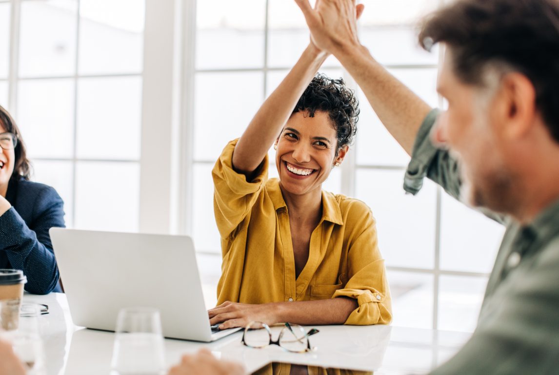 Business people celebrating success in an office. Happy business professionals doing a high five during a meeting. Teamwork and goal achievement.